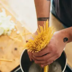 Hände mit Tattoos halten Spaghetti über einen Topf. Das bedeutet al dente: perfekt gekochte Pasta.