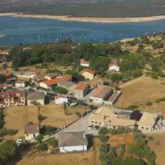 Vista aérea de Cervera de Buitrago, con casas de tejados naranjas y un embalse azul al fondo.