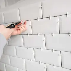 Pose de carrelage blanc avec des croisillons pour assurer un espacement parfait. Un outil est utilisé pour ajuster le **taille croisillon carrelage**.