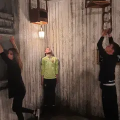 Trois personnes dans une pièce aux murs décrépits, défiant la gravité. Une femme s'accroche à un mur, un homme flotte, un autre escalade une chaise. Ambiance de **the dark dreams Paris**.