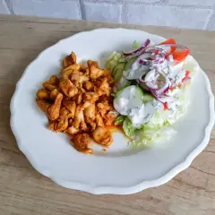Talerz z porcją pikantnego kurczaka i świeżą sałatką z pomidorów, ogórka i cebuli. Tak wygląda shoarma co to za danie!