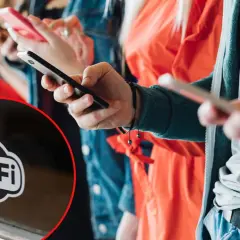 Ludzie korzystają z telefonów, a na pierwszym planie widać symbol Wi-Fi, sugerujący darmowy internet.