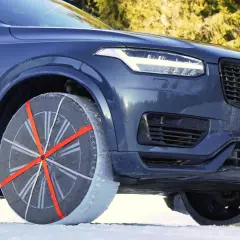 Un coche oscuro con cadenas textiles en la rueda delantera, listo para circular sobre nieve o hielo.
