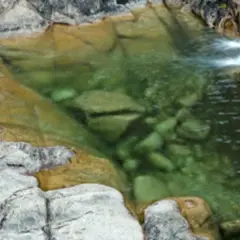 Senderista se detiene junto a un **río caldo** de aguas cristalinas y rocas musgosas.
