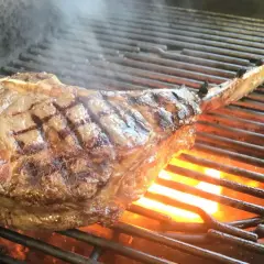 Ein saftiges Tomahawk Steak grillen, mit sichtbaren Grillstreifen und Flammen darunter.
