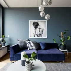 Ein tiefes, modernes Blau dominiert diesen Wohnraum. Ein Samtsofa in diesem Farbton lädt zum Entspannen ein, während ein Kunstwerk und geometrische Lampen Akzente setzen.