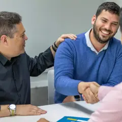 Hombres estrechando manos y sonriendo. Uno pone una mano en el hombro del otro, como si cerraran un trato importante, quizás sobre cómo es obligatorio tener seguro de hogar.
