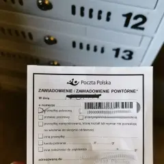 Zawiadomienie z Poczty Polskiej o przesyłce poleconej. W tle widoczne skrzynki pocztowe z numerami 12 i 13.