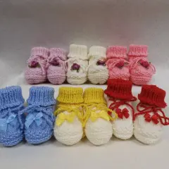 Una fila di babbucce neonato ai ferri rosa, bianche, gialle e rosse, alcune con fiocchi e decorazioni floreali, pronte per scaldare i piedini più piccoli.