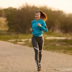 Uśmiechnięta kobieta w sportowym stroju biegnie po asfaltowej ścieżce. Zastanawia się, jakie tetno podczas biegu jest optymalne.