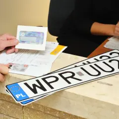 Ręce klienta pokazują dokumenty i nowe tablice rejestracyjne WPR UU22, gotowe do odbioru po załatwieniu formalności.