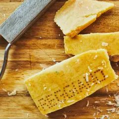 Des morceaux de **croûte parmesan comestible** sur une planche en bois, avec un râpe à fromage.