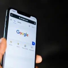 Dłoń trzyma smartfon z otwartą stroną Google. Widać pasek wyszukiwania i opcje takie jak pogoda, sport, filmy, restauracje, idealne do odkrywania treści w Google Discover.