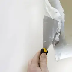Dłoń z kielnią nakłada gips na białą ścianę.