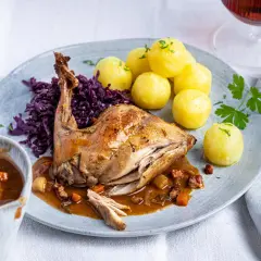 Rezept Hasenbraten im Backofen: Saftiges Kaninchen mit Klößen, Rotkohl und Sauce auf einem Teller.