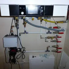 Podłączenie pieca gazowego kondensacyjnego. Widoczny panel sterowania, pompa, zawory i rury tworzące skomplikowaną instalację grzewczą.