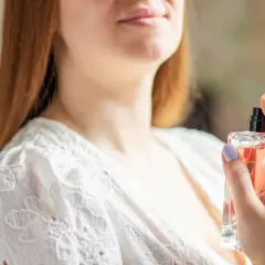 Kobieta z rudymi włosami rozpyla perfumy z buteleczki.