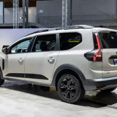 Biały samochód Dacia Jogger widziany z boku, z tyłu, na tle hali wystawowej.