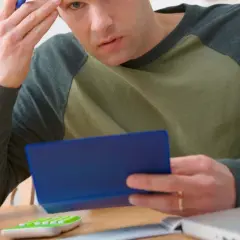 Homme pensif, calculatrice, tasse verte, ordinateur portable. Il se demande combien de temps garder chéquier.