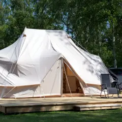 Stor glampingtält i Mölle med träaltan och solstolar. En bil syns i bakgrunden.