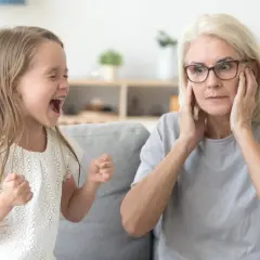 Rozkrzyczane dziecko nie może usiedzieć w miejscu, a babcia zakrywa uszy, próbując zapanować nad chaosem.