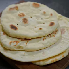 Pile de pains arabes moelleux, légèrement dorés par la cuisson, sur une planche en bois. Parfait pour accompagner un repas.