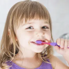 Bambina sorridente si lava i denti con un dentifricio al fluoruro di sodio per un sorriso smagliante.