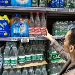 Une femme choisit une bouteille d'eau minérale Badoit. Les étiquettes indiquent la composition et le prix.