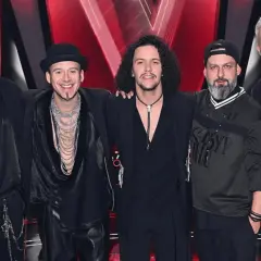 Pięciu mężczyzn w czarnych strojach, przypominających styl zespołu Afromental, pozuje na tle sceny.