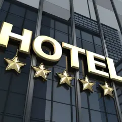 Złoty napis HOTEL z pięcioma gwiazdkami na tle nowoczesnego budynku hotelowego.