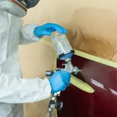 Osoba w kombinezonie ochronnym i masce maluje samochód pistoletem. Czy to terpentyna co to za rozpuszczalnik?