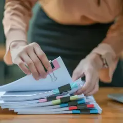 Ręce sortują dokumenty z kolorowymi spinaczami. Czy to rachunki, czy może coś związanego z fiskusem?