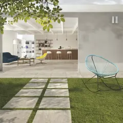 Un sentiero in lastre quadrate su prato verde conduce a un'area living con pavimentazione esterna moderna, che si apre su un interno luminoso con cucina e soggiorno.