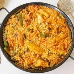 Paella de pollo recién hecha, con trozos de pollo dorado, judías verdes y arroz sabroso en una paellera.