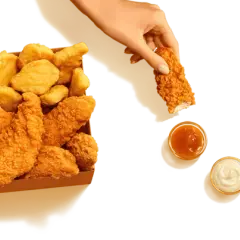 Pudełko McDonald's z kurczakiem i frytkami. Ręka zanurza kawałek kurczaka w sosie. Sprawdź kcal!