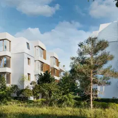 Nowoczesna sopocka architektura, białe budynki z drewnianymi elementami i dużymi oknami, otoczone zielenią.