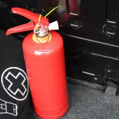 Czerwona gaśnica śniegowa, idealna do gaszenia pożarów cieczy palnych i urządzeń elektrycznych, gotowa do akcji w bagażniku.
