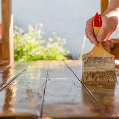Mano aplicando barniz a una mesa de madera. El proceso de lijar después de barnizar es clave para un acabado perfecto.