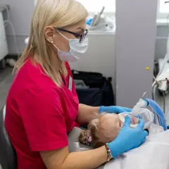 Dentystka w masce zakłada dziecku maskę znieczulającą. Obserwacja objawów uczulenia na znieczulenie u dentysty jest kluczowa.