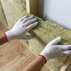 Mani guantate posizionano materiale isolante per un cappotto interno fai da te.