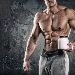 Muscoloso bodybuilder con addominali scolpiti tiene un barattolo bianco, simbolo di un efficace schema integrazione bodybuilding.