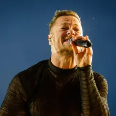 Wokalista Imagine Dragons śpiewa do mikrofonu na tle błękitnego nieba.