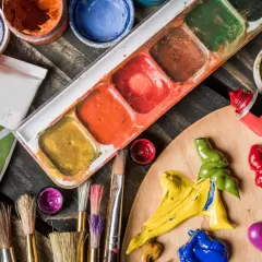 Palette d'un artiste peintre acrylique avec tubes de peinture, pinceaux et godets de couleurs vives sur fond de bois.