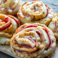 Roladki z ciasta na pizzę z serem i wędliną, ułożone na desce.