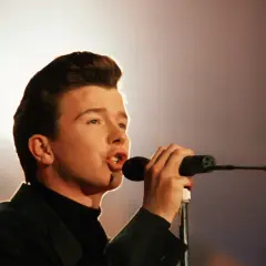 Junger Rick Astley singt mit Leidenschaft ins Mikrofon, sein ikonischer Look ist bereits erkennbar.
