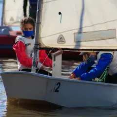 Dwie dziewczynki w maskach na twarzach żeglują małą łodzią.