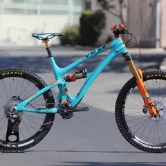 A turquoise Yeti SB6c mountain bike with orange accents, featuring Maxxis tires and Fox suspension, ready for any trail.