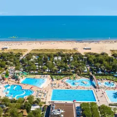 Widok z lotu ptaka na plażę i kompleks basenów w **marina do Venezia**. Widać morze, piaszczystą plażę z leżakami, camping i zjeżdżalnie wodne.