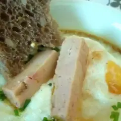 Œuf cocotte au foie gras, servi avec une tranche de pain aux céréales et des herbes fraîches. Un délice pour le palais.