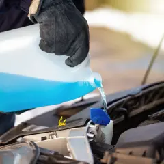 Persona con guantes vierte líquido azul de un bidón en el depósito del limpiaparabrisas. Es lo mismo refrigerante que anticongelante.